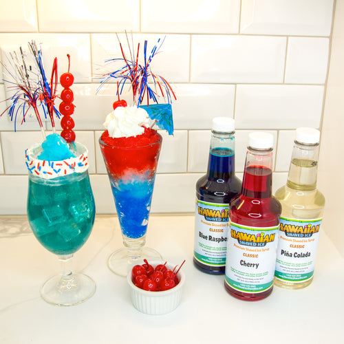 Front facing image of three 16-oz pints, flavors Cherry (Red), Blue Raspberry (Blue), and Pina Colada (Clear). To the left of the pints are two Fourth of July-themed drinks (Red, White, and Blue), and a small white bowl with cherries.
