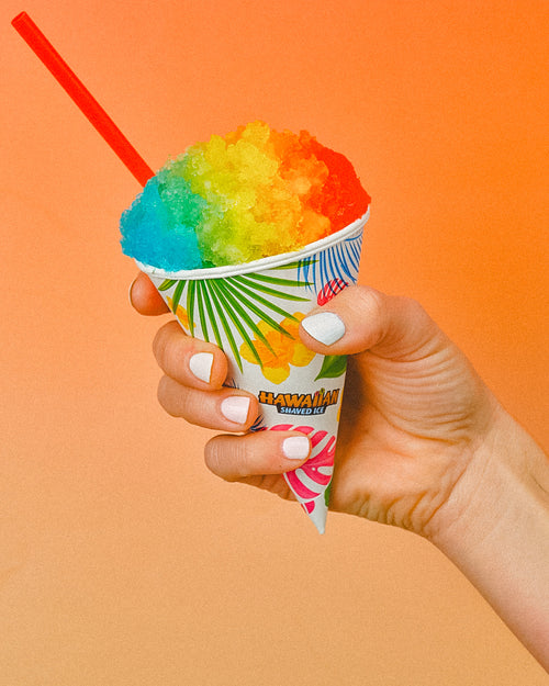 Hand holding a colorful snow cone with a red straw against an orange background
